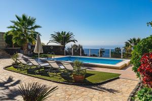 a swimming pool with chairs and an umbrella and the ocean at Luxusvilla Sol y Mar mit grandiosem Meerblick in Adeje