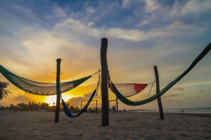 a hammock on the beach with the sunset in the background at Aimberê Eco Resort Hotel in Coqueiro