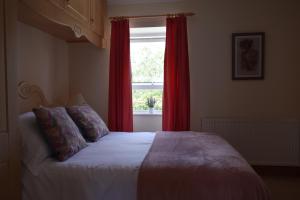 1 dormitorio con 1 cama con cortinas rojas y ventana en Teach Kitty Con en Dungloe