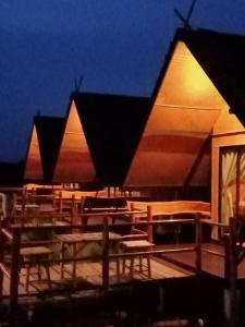 a group of tables and chairs on a deck at night at บ้านนอก คอกนา คาเฟ่ เพชรบุรี in Ban Tha Kham