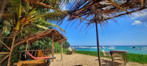 a beach with a hut and chairs and the ocean at Kusuma's Lazy Left in Midigama East