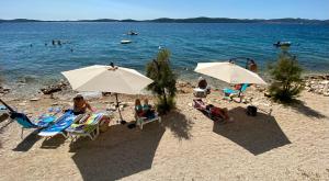a group of people sitting on a beach with umbrellas at Olea Apartments in Bibinje
