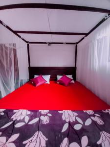 a bed in a room with red sheets and pillows at Rainforest River Bay in Deniyaya