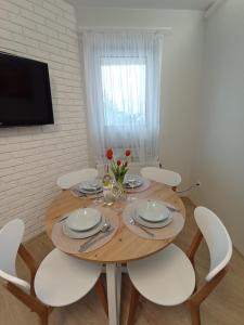 uma mesa de jantar com cadeiras brancas e uma televisão em Apartament Primo Darłówko em Darłowo