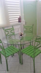 un tavolo in vetro con due sedie verdi e un tavolo con una ciotola di fiori di Résidence rose Cannelle a Grand-Bourg