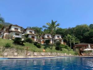 Residência em condom, 1 ou 2 suítes, vista para o mar, Praia do Curral, Ilhabela في إلهابيلا: مسبح في منتجع فيه كراسي وشقق