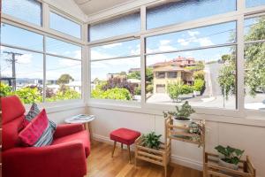 ein Wohnzimmer mit großen Fenstern und einem roten Stuhl in der Unterkunft Warwick St Retreat! 3 Bedroom House With Parking in Hobart