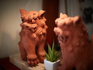 duas estátuas de gatos e um vaso de planta sobre uma mesa em 民宿さざんか em Okinawa