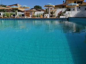 a large swimming pool with blue water and umbrellas at Le Palme Holidays in Palmadula