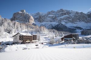 a building in the snow next to a mountain at Hotel Plan De Gralba - Feel the Dolomites in Selva di Val Gardena