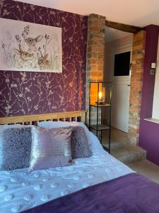 1 dormitorio con 1 cama con pared morada en Wisteria Cottage - Hillside Holiday Cottages, Cotswolds, en Warmington