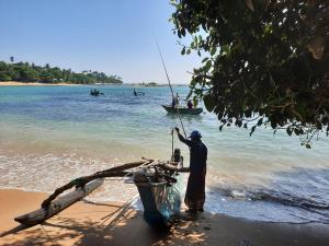 a man standing on the beach with a boat in the water at Eagle Homestay in Tangalle