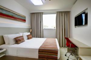 1 dormitorio con 1 cama blanca, escritorio y ventana en Transamerica Fit Vitória Reta da Penha, en Vitória