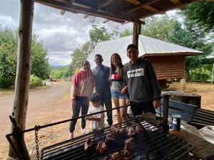 a group of people standing around a grill with meat at Ruka Huilipan in Nueva Imperial