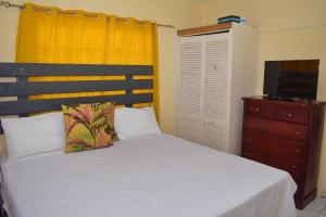 a bedroom with a bed and a dresser and a television at Unity Villa 3 bedroom with fans Wifi Parking in Montego Bay