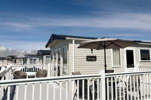 eine Veranda mit Stühlen und einem Regenschirm auf einem Haus in der Unterkunft The Sea Breeze - 8 Berth Premium Caravan in Camber Sands in Camber