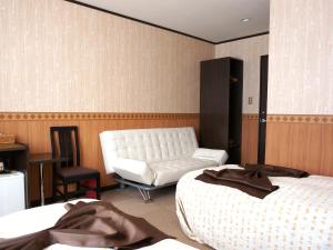 a hotel room with two beds and a white couch at Petit Hotel Blaneneige in Nakafurano