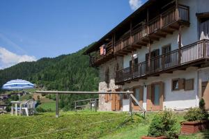 a building with a balcony and an umbrella on a hill at CASA BERNARD Zortea VANOI cuore verde del Trentino in Canale San Bovo