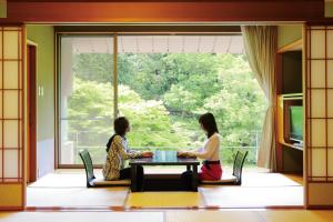 Zwei Frauen sitzen an einem Tisch vor einem Fenster in der Unterkunft Sora Togetsusoukinryu in Izu