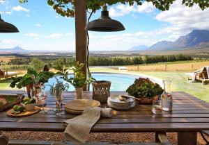 una mesa de madera con platos de comida y una piscina en BoPlaas Country Cottages, en Wellington