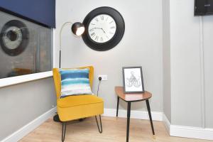 a yellow chair and a table with a clock on the wall at Elm House by YourStays in Crewe