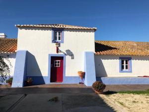 a white house with a red door in a yard at Quinta do Sardanito de Tras in Zambujeira do Mar