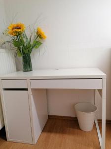 een wit bureau met een vaas met bloemen erop bij D&E Rooms in Schwechat