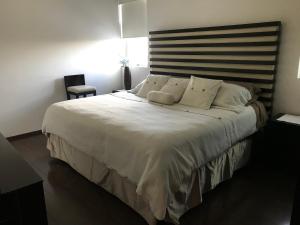 um quarto com uma cama grande com lençóis brancos e almofadas em Habitación confortable dentro departamento Natura em Cidade do México