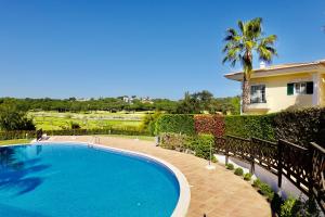 a swimming pool in front of a house with a palm tree at Villa Formosa Golf in Quinta do Lago