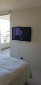 TV de pantalla plana colgada en una pared junto a la cama en Departamento nuevo con la mejor ubicación, en Viña del Mar