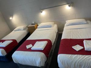 three beds in a room with white and red at Lake Munmorah Motel in Lake Munmorah