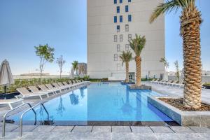 a hotel swimming pool with chairs and a palm tree at Ideal 1BR at The Pulse Residence Icon A1 Dubai South by Deluxe Holiday Homes in Dubai