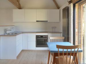 a kitchen with white cabinets and a blue table and chairs at High Cogges Farm Holiday Cottages - The Granary in Witney