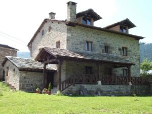 una antigua casa de piedra con un porche de madera en un campo en Posada La Braniza, en Vega de Pas