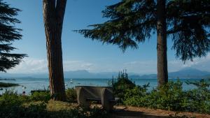 a bench sitting between two trees next to the water at Hotel Bella Italia in Peschiera del Garda