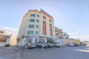 a large building with cars parked in a parking lot at Super OYO 111 Al Thabit Hotel in Sur