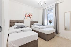 two beds in a white room with a window at Spacious home with parking - TV in Every Bedroom! in Swansea
