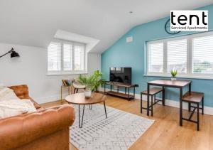 Stylish & Comfy 1 Bed Apt by Tent Serviced Apartments Egham - Town centre with parking and Wifi في ايجهام: غرفة معيشة مع جدران زرقاء وأريكة وطاولات