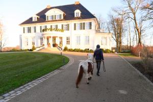Una donna che cammina a cavallo davanti a una casa di Hotel Gut Immenhof a Malente