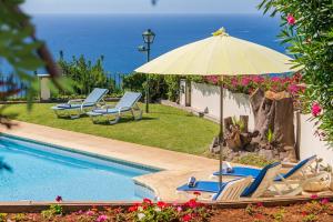 ein Pool mit Stühlen und einem Sonnenschirm und das Meer in der Unterkunft OurMadeira - Villa Vista Sol, grand traditional in São Gonçalo
