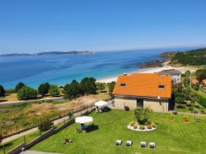 an orange roofed house on a green field with the ocean at Apartamentos Rozas Vellas in Sanxenxo