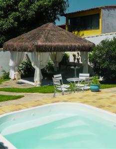 una piscina con sombrilla de paja, mesa y sillas en Estrela Azul Guest House Búzios, en Búzios