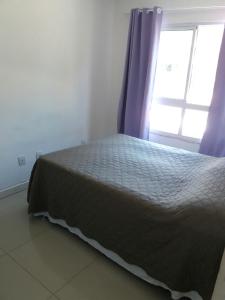 1 dormitorio con 1 cama con cortinas moradas y ventana en Canasvieiras - Residencial Costa do Mar, en Florianópolis