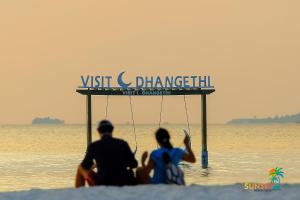 two people sitting on the beach in the water at Sunset Beach View in Dhangethi