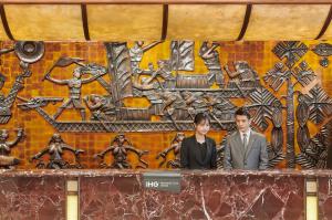 Crowne Plaza Zhuhai City Center, an IHG Hotel في تشوهاى: رجلان يقفان على منضدة أمام لوحة جدارية