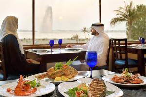 zwei Personen sitzen an einem Tisch mit Teller Essen in der Unterkunft Al Corniche in Dschidda