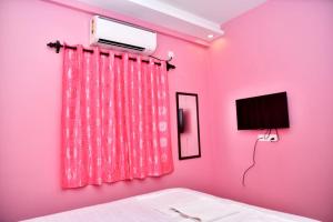 Habitación de color rosa con cama y TV en INDRAYANI GUEST HOUSE, en Calangute