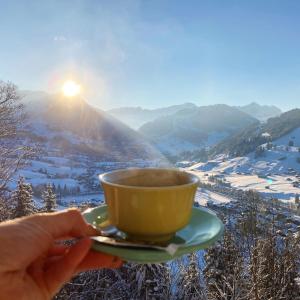 a person holding a cup of coffee in front of a mountain at The Sun&Soul Panorama Pop-Up Hotel Solsana in Gstaad