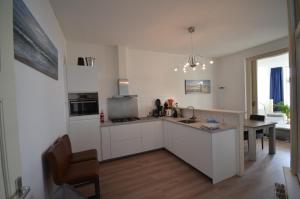 a kitchen with white cabinets and a table in it at Fraai appartement direct aan zee op toplocatie. in Vlissingen +10 photos