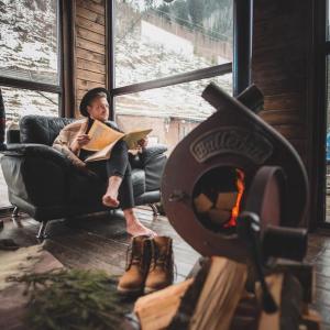 un hombre sentado en una silla leyendo un libro junto a una chimenea en 4 Mountains Hotel en Bystrets